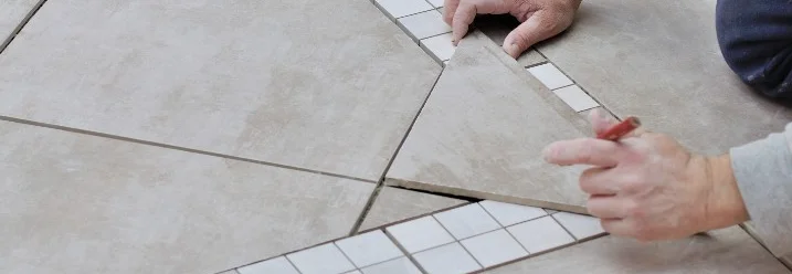 Person verlegt Fliesen und macht Markierungen mit einem Bleistift